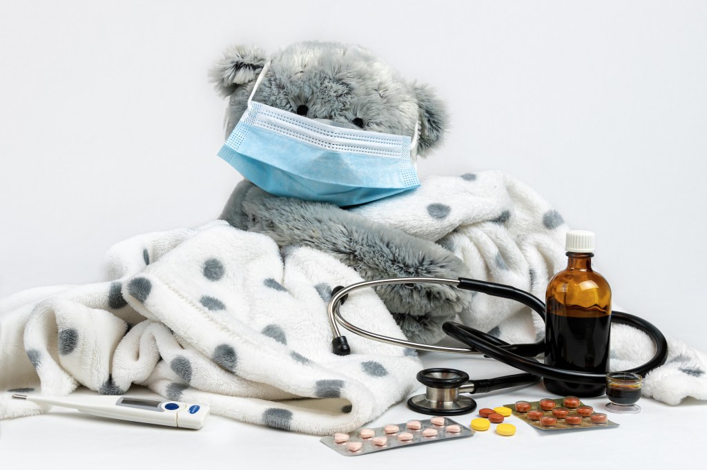 Sick teddy bear with face mask, thermometer and cold medicine — home care for a child with cold and fever